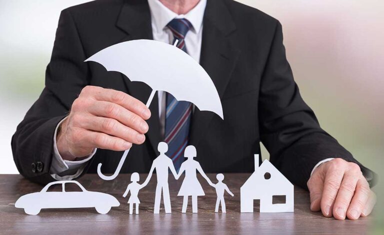 A young family reviews finances together at their dining table with insurance documents and a laptop.