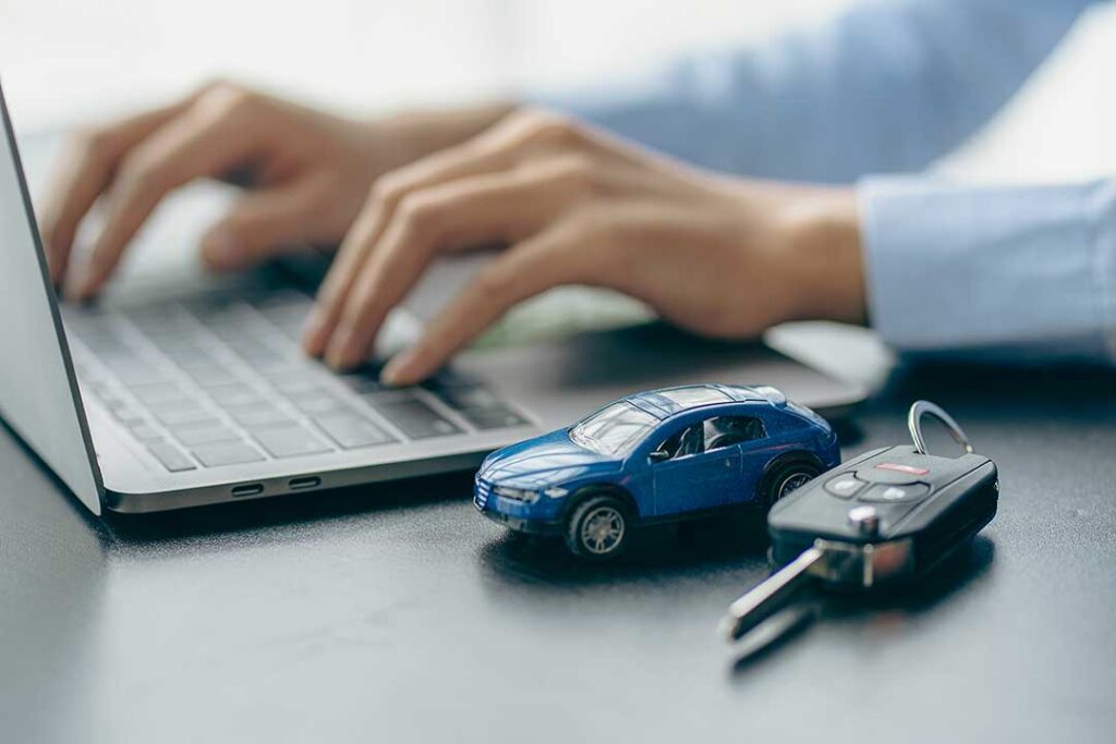 A person reviews a car insurance policy at a kitchen table with keys and a vehicle registration nearby.